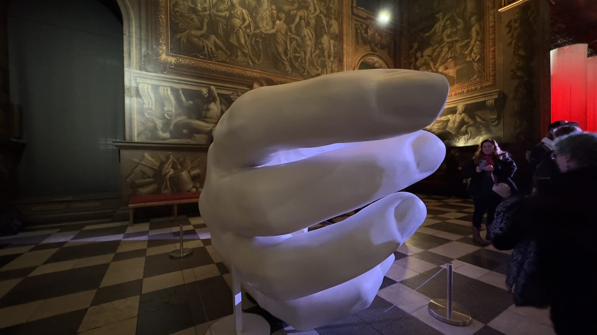 Grande main sculptée de Peter Walker illuminée dans le Painted Hall, sur fond de fresques baroques et de sol en damier